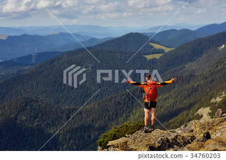 Hiker with backpack standing on top of a mountain 34760203