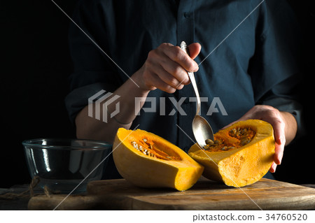 Spoon in hand, pumpkin halves on a table on a blue 34760520