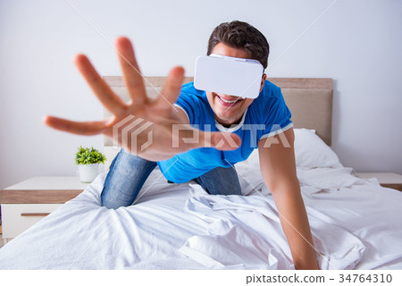 Young man in bed wearing a vr virtual reality head 34764310