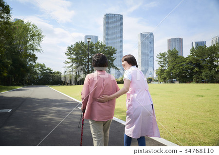 Back view of senior and helper taking a walk with a cane Back view of senior and helper taking a walk with a cane 34768110