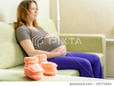 Baby shoes on the couch next to a pregnant woman 34772640