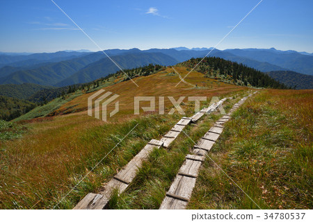 在Aizu Komagatake Koma的小屋和遠處的陽光山下的草秋葉的斜坡 34780537