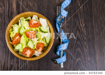 Salad in wooden bowl and measuring tape  34783340