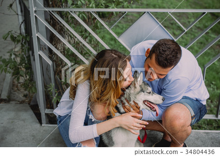 Beautiful young couple playing with a dog husky Beautiful young couple playing with a dog husky 34804436