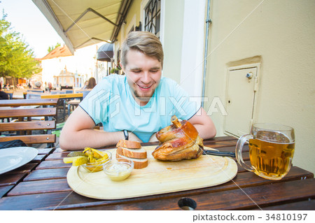 Young man eating smoked pork leg meat and drinking Young man eating smoked pork leg meat and drinking 34810197