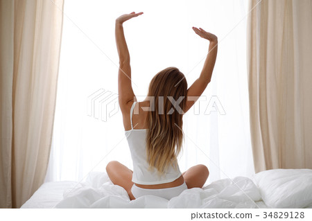 Woman stretching in bed after wake up, back view Woman stretching in bed after wake up, back view 34829128