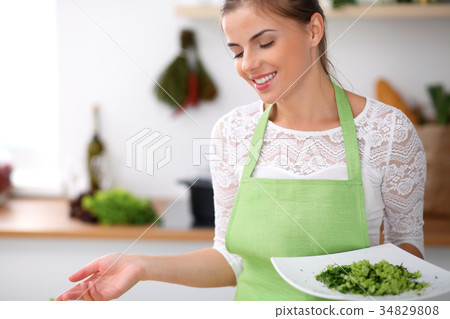 Young woman in green apron is cooking in a kitchen Young woman in green apron is cooking in a kitchen 34829808