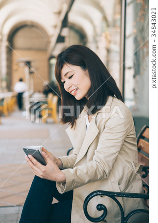 Woman watching smartphone while drinking coffee on a bench 34843021