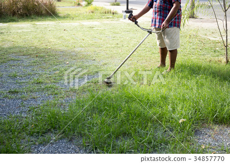 Senior worker mow grass with electric hand trimmer 34857770