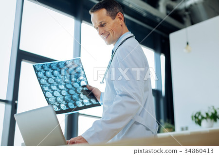 Joyful smart doctor holding an X ray photo Joyful smart doctor holding an X ray photo 34860413