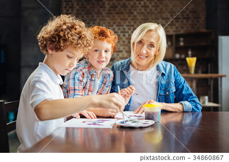 Kind elderly lady painting with grandsons at table Kind elderly lady painting with grandsons at table 34860867