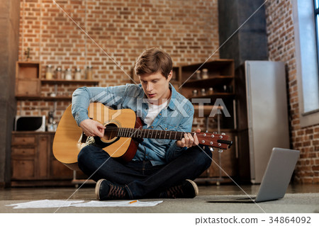 Young man playing guitar and reading music sheet Young man playing guitar and reading music sheet 34864092