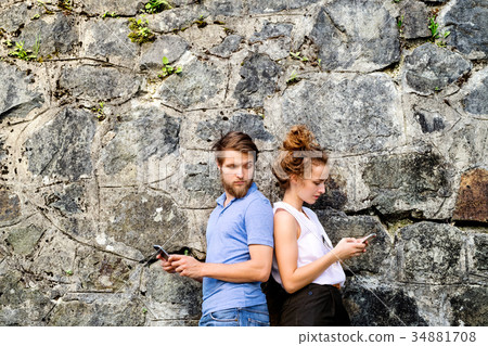 Young couple with smartphones against stone wall Young couple with smartphones against stone wall 34881708