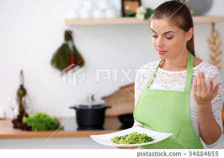 Young woman in green apron is cooking in a kitchen 34884655