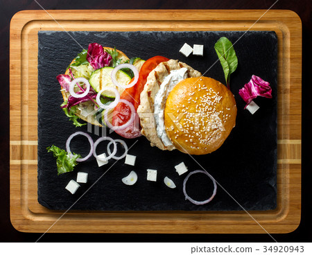 Open hamburger lies on the slate tile. 34920943