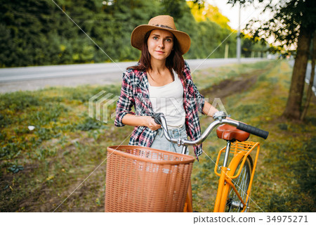 Woman in hat against vintage bicycle with basket Woman in hat against vintage bicycle with basket 34975271