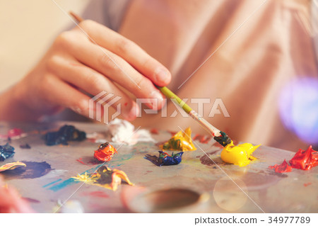 Close up of child mixing oil paints on palette 34977789