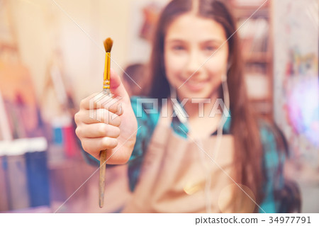 Smiling girl posing with painting brush for camera Smiling girl posing with painting brush for camera 34977791