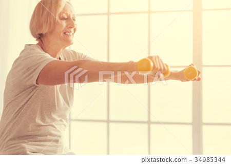 Positive aged woman exercising wuth dumbbells Positive aged woman exercising wuth dumbbells 34985344