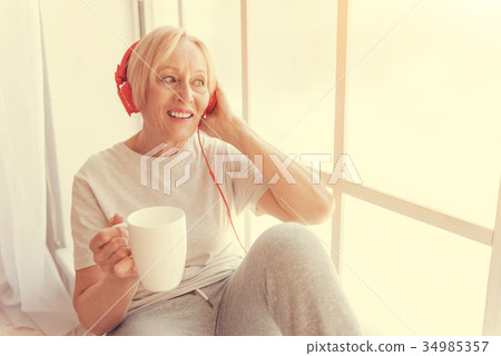 Cheerful aged woman resting on the window sill Cheerful aged woman resting on the window sill 34985357