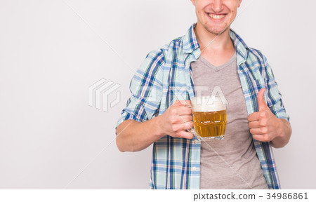 Close up of young man holding beer mug and showing 34986861