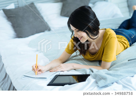 Joyful young brunette taking notes in bed 34988758