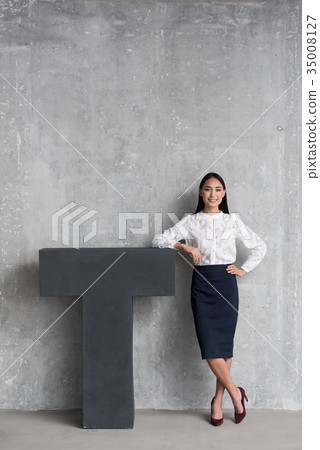 Cheerful businesswoman standing near big T 35008127