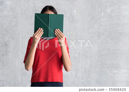 Charming young woman is covering behind storybook Charming young woman is covering behind storybook 35008420