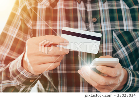 young man holding credit card and use smartphone young man holding credit card and use smartphone 35025034