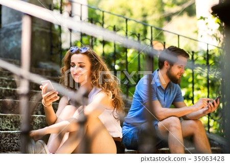 Young couple with smartphones sitting on stairs in Young couple with smartphones sitting on stairs in 35063428