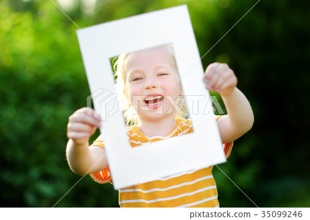 Cute cheerful little girl holding white picture frame in front of her face 35099246
