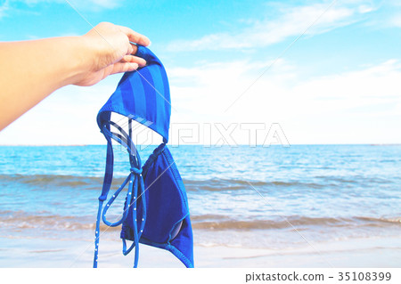 Woman hand holding bikini with sea and blue sky Woman hand holding bikini with sea and blue sky 35108399