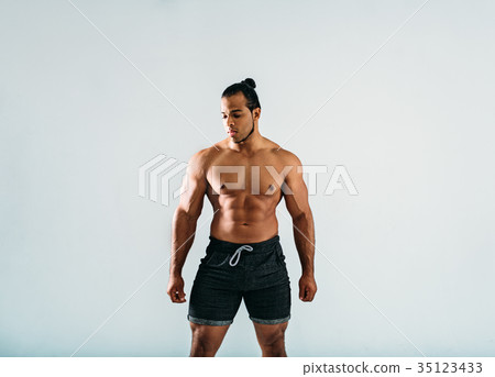 Male bodybuilder posing in studio, looking away Male bodybuilder posing in studio, looking away 35123433