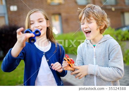 Two funny friends playing with fidget spinners on the playground 35124388