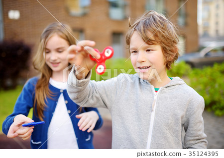 Two funny friends playing with fidget spinners on the playground 35124395