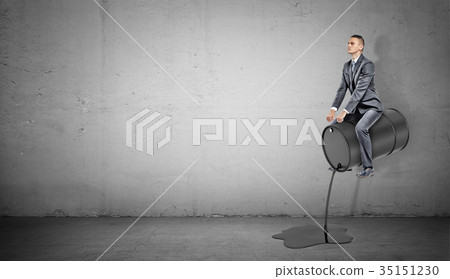 A small businessman sits on a black barrel leaking A small businessman sits on a black barrel leaking 35151230