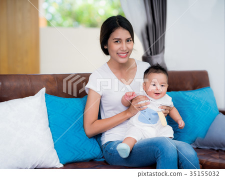 Mom and newborn baby sit and play togather on sofa 35155032