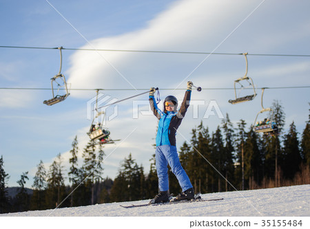 Female skier against ski-lift and forest on a sunny day Female skier against ski-lift and forest on a sunny day 35155484