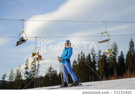 Female skier against ski-lift and forest on a sunny day Female skier against ski-lift and forest on a sunny day 35155485