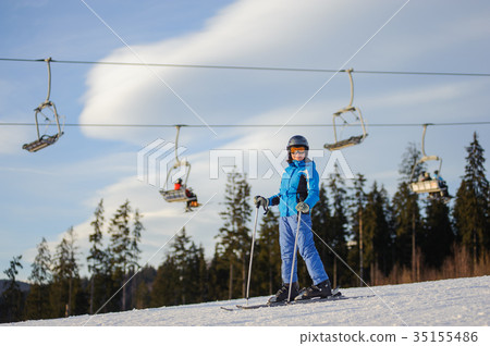 Female skier against ski-lift and forest on a sunny day Female skier against ski-lift and forest on a sunny day 35155486