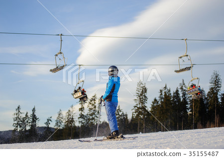 Female skier against ski-lift and forest on a sunny day Female skier against ski-lift and forest on a sunny day 35155487