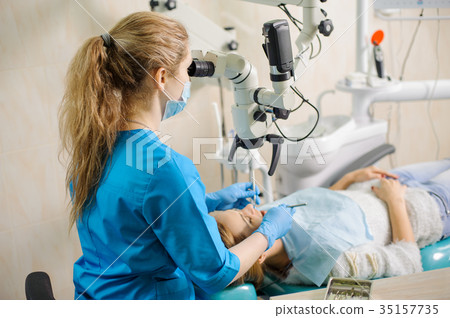 Female dentist treating caries using microscope at the dentist office Female dentist treating caries using microscope at the dentist office 35157735
