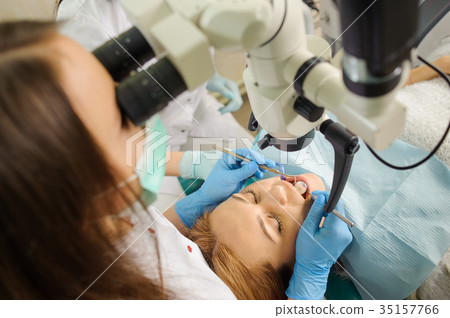 Female dentist treating caries using microscope at the dentist office 35157766