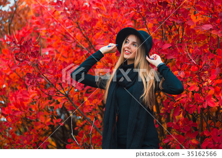 Elegant blonde woman standing in a park in autumn Elegant blonde woman standing in a park in autumn 35162566