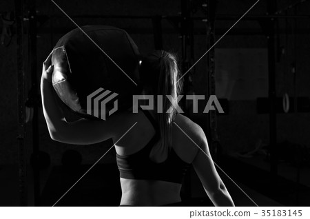 Muscular woman working out in gym with heavy ball 35183145