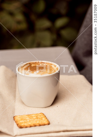 White cup of cappuccino and cracker on napkin White cup of cappuccino and cracker on napkin 35187009