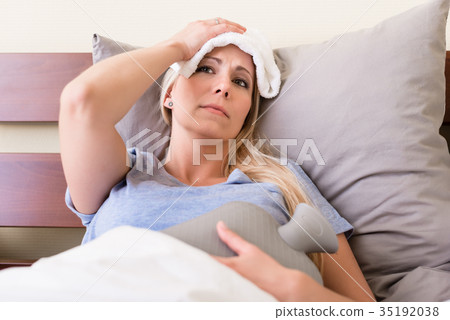 Young sick woman with fever lying in bed Young sick woman with fever lying in bed 35192038