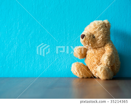 The brown teddy bear sitting on wood table. 35214365