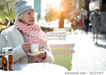 Pensive mature lady sitting outside with mug of Pensive mature lady sitting outside with mug of 35215457