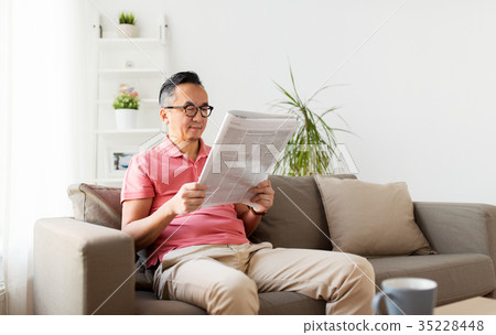 asian man in glasses reading newspaper at home 35228448